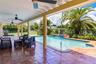 Covered patio with terracotta tile flooring, ceiling fans, in-ground swimming pool, integrated spillover spa, and mature landscaping