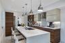 Kitchen featuring a waterfall-edge center island, wood-finish cabinetry, light-toned solid surface countertops, stainless steel pendant lighting, and 
