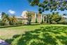 Two-story exterior featuring a columned front portico, light-toned stucco siding, and meticulously manicured hedging on an expansive lawn with mature 