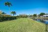 Backyard featuring a manicured lawn, perimeter hedge, chain-link fencing, palm trees, and waterfront access