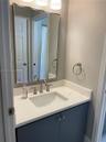 Bathroom vanity featuring a stone-composite countertop with integrated sink, polished chrome widespread faucet, navy blue cabinetry, and a framed rect