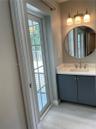 Vanity featuring a solid-surface countertop, integrated rectangular sink, dark cabinetry with hardware, a circular wall-mounted mirror, and a three-li