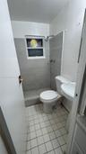 Bathroom featuring a walk-in shower with grey horizontal tile surround, a pedestal sink, a standard-height toilet, and square ceramic floor tiling