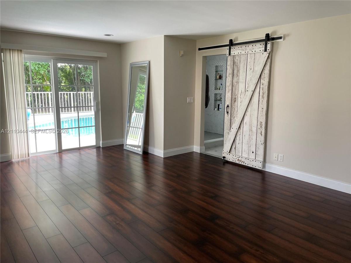 Dark wood-finish flooring, sliding glass door with exterior pool access, and distressed white-finish barn door with matte black hardware