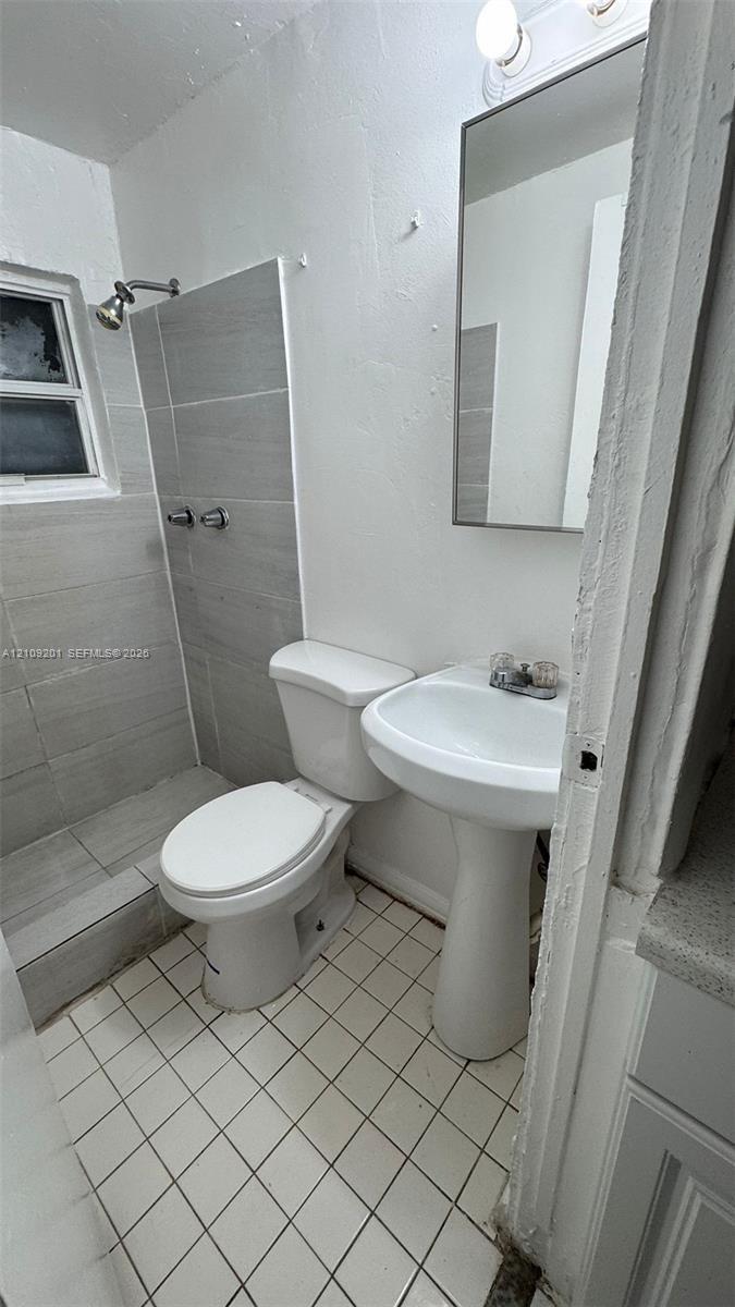 Bathroom featuring a walk-in shower with grey horizontal tiling, white pedestal sink, tiled flooring, and a wall-mounted rectangular mirror