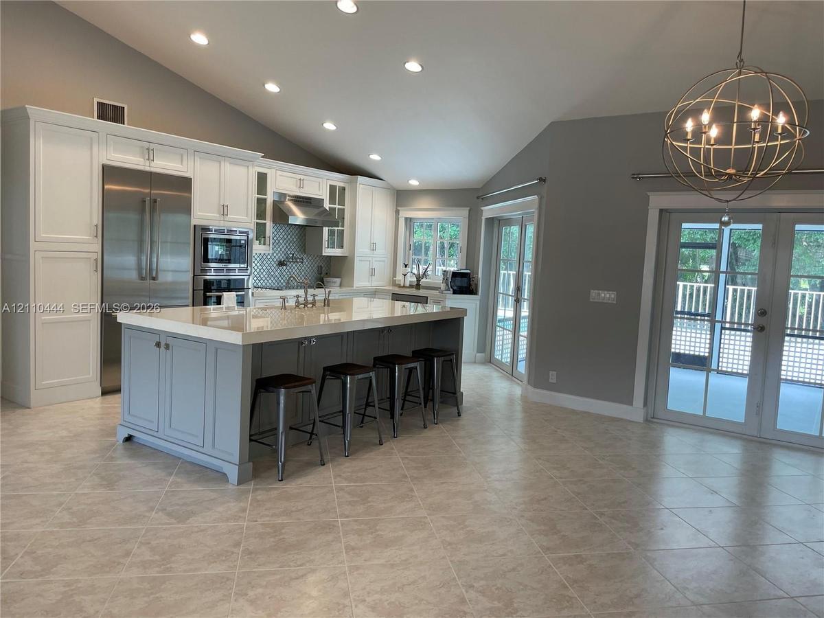 Kitchen featuring an oversized central island with stone-finish countertops, stainless steel appliances, vaulted ceilings, recessed lighting, and glas