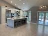 Kitchen featuring an oversized central island with stone-finish countertops, stainless steel appliances, vaulted ceilings, recessed lighting, and glas