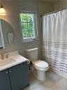 Bathroom featuring a charcoal-toned vanity with a white countertop, circular wall-mounted mirror, single-handle brushed nickel faucet, and wood-finish