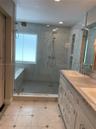Walk-in shower featuring glass paneling, floor-to-ceiling tile, and built-in shelving, paired with a dual-sink vanity with stone-finish countertops an