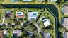 Aerial perspective of a waterfront lot featuring extensive canal frontage, an in-ground swimming pool, a paved driveway, and mature landscaping