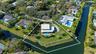 Aerial view of a waterfront property featuring a canal-front lot, a private swimming pool, a sprawling lawn, and mature perimeter landscaping