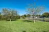 Expansive lawn featuring mature trees, chain-link fencing, and water frontage