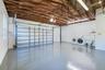 Multi-vehicle garage featuring an exposed wood-beam ceiling, finished epoxy flooring, a sectional roll-up door, and a built-in utility sink