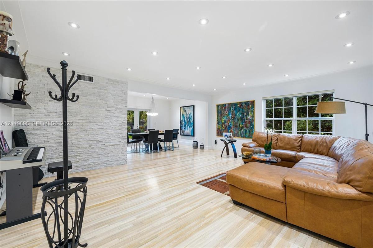 Open-concept interior featuring wood-finish flooring, a floor-to-ceiling stacked stone feature wall, recessed lighting, and multi-pane windows