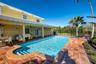 Covered patio with recessed lighting and ceiling fans, red tile pool deck, in-ground pool with integrated steps, and raised spa with brick surround
