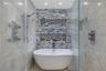 Freestanding soaking tub with polished chrome fixtures, integrated stacked-stone feature wall with dual recessed shelving, stone pebble flooring, and 
