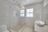 Bathroom featuring a glass-enclosed walk-in shower with pebble-stone flooring, a wall-mounted rainfall showerhead, a quartz-topped vanity with an oval