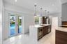 Kitchen featuring a waterfall-edge quartz island, wood-finish cabinetry, recessed lighting, stone-finish flooring, and glass-paneled double doors