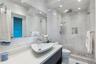 Bathroom featuring full-height stone-finish wall tile, frameless glass shower enclosure, recessed shower niche, vessel sink with chrome hardware, and 