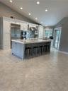 Kitchen featuring an oversized island with quartz countertops, custom cabinetry, stainless steel appliances, tile flooring, and vaulted ceilings with 