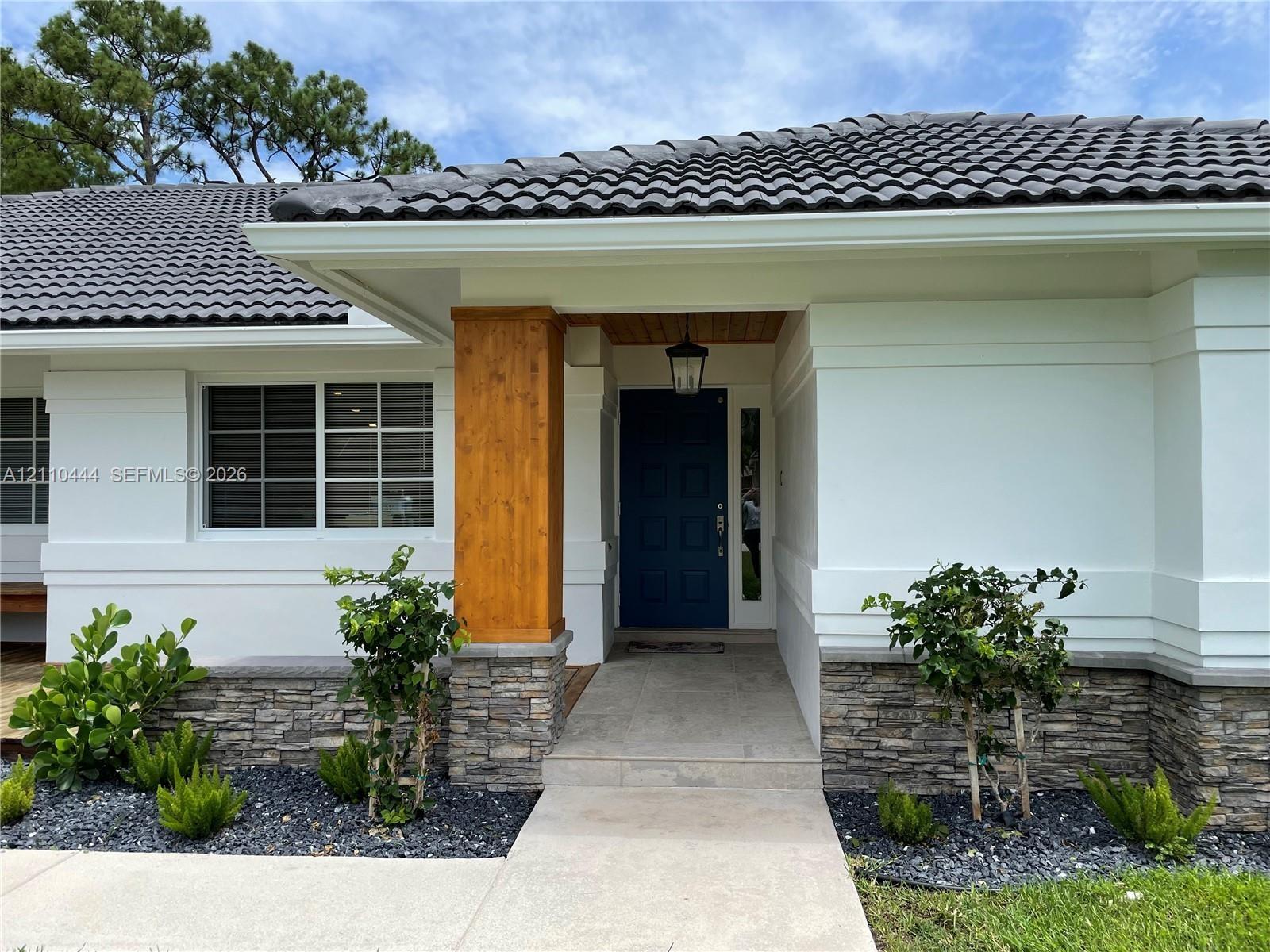 Exterior featuring a dark tile roof, smooth-finish white facade, stone veneer accents, prominent wood-finish support pillar, and a solid-panel front d