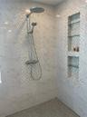 Walk-in shower featuring large-format stone-patterned wall tiles, decorative mosaic accent tiling, a rainfall showerhead with a handheld sprayer, and 