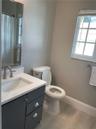 Bathroom featuring a vanity with dark cabinetry, stone-finish countertop, undermount sink, and arched-spout faucet, complemented by wood-finish floori