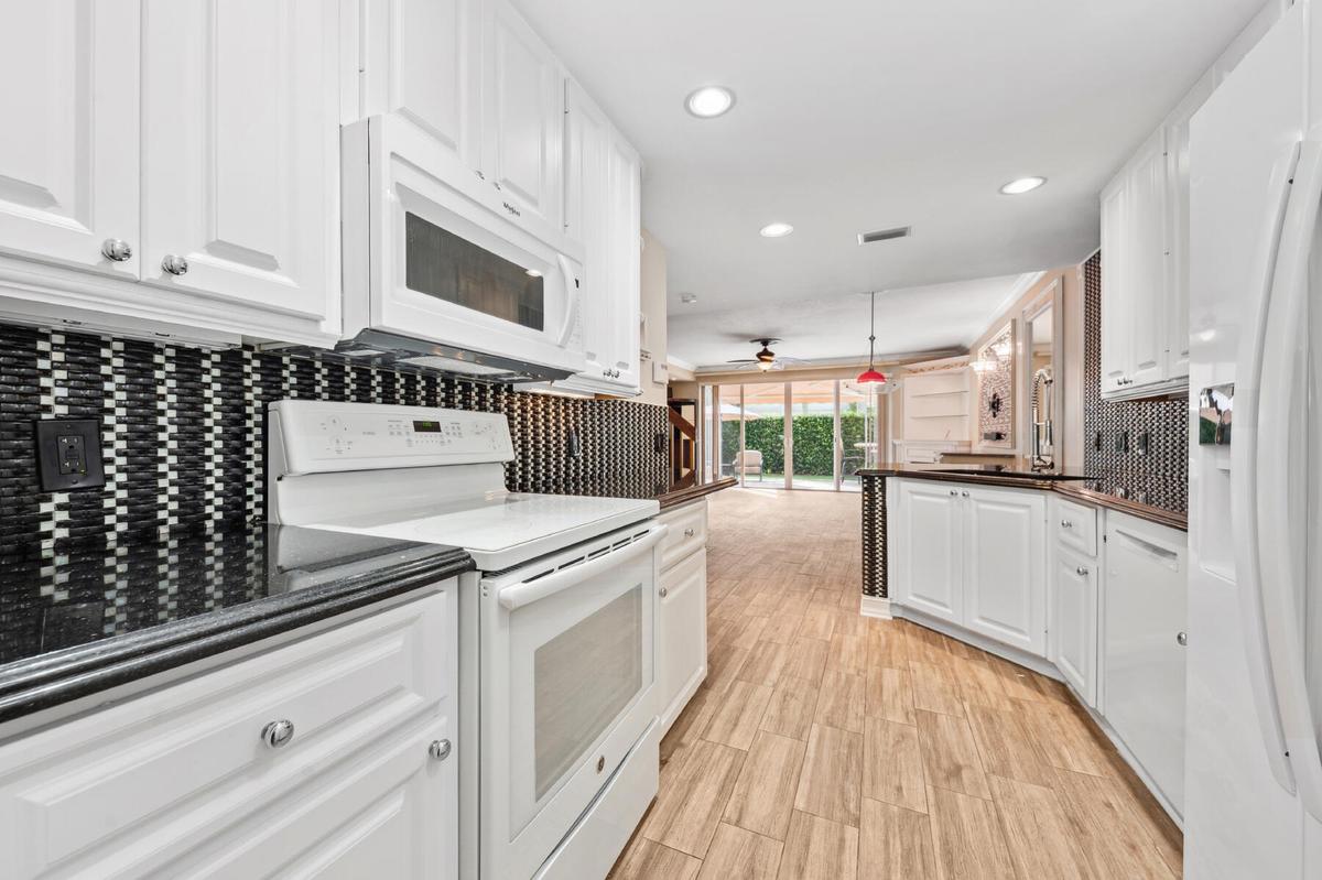 Kitchen featuring white cabinetry, dark countertops, a geometric mosaic tile backsplash, wood-finish flooring, and recessed lighting