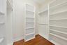Custom walk-in closet featuring floor-to-ceiling white shelving units, integrated hanging rods, and wood-finish flooring