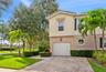 Two-story residence featuring a paved stone driveway, single-car garage, stucco exterior, accent shutters, and circular window detailing