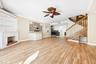 Wood-finish flooring, fireplace with stone-tile surround, custom built-in cabinetry, decorative ceiling fan, and wooden staircase with metal balusters