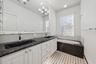 Dual-sink vanity with stone-finish countertops, undermount sinks, white cabinetry, integrated soaking tub, and decorative wall-to-wall mirror with fra