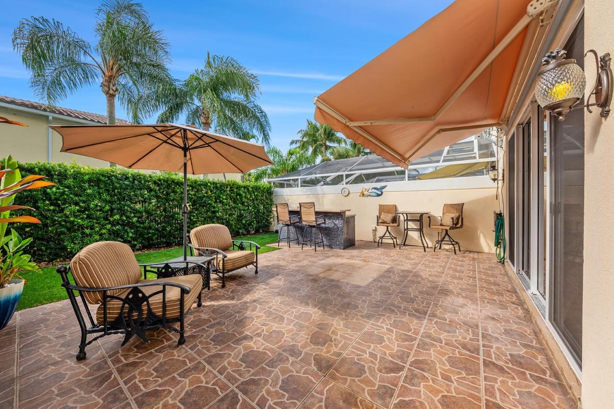 Outdoor patio featuring stone-patterned tile, a built-in stone-finished wet bar, a retractable awning, and integrated wall-mounted lighting