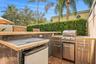 Outdoor kitchen featuring stainless steel cabinetry, a built-in grill, stone-tiled bar counter, and mosaic tile detailing