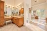 Bathroom featuring wood-finish cabinetry with a vanity station, stone-surfaced countertop, tile flooring, glass-enclosed shower, and a soaking tub