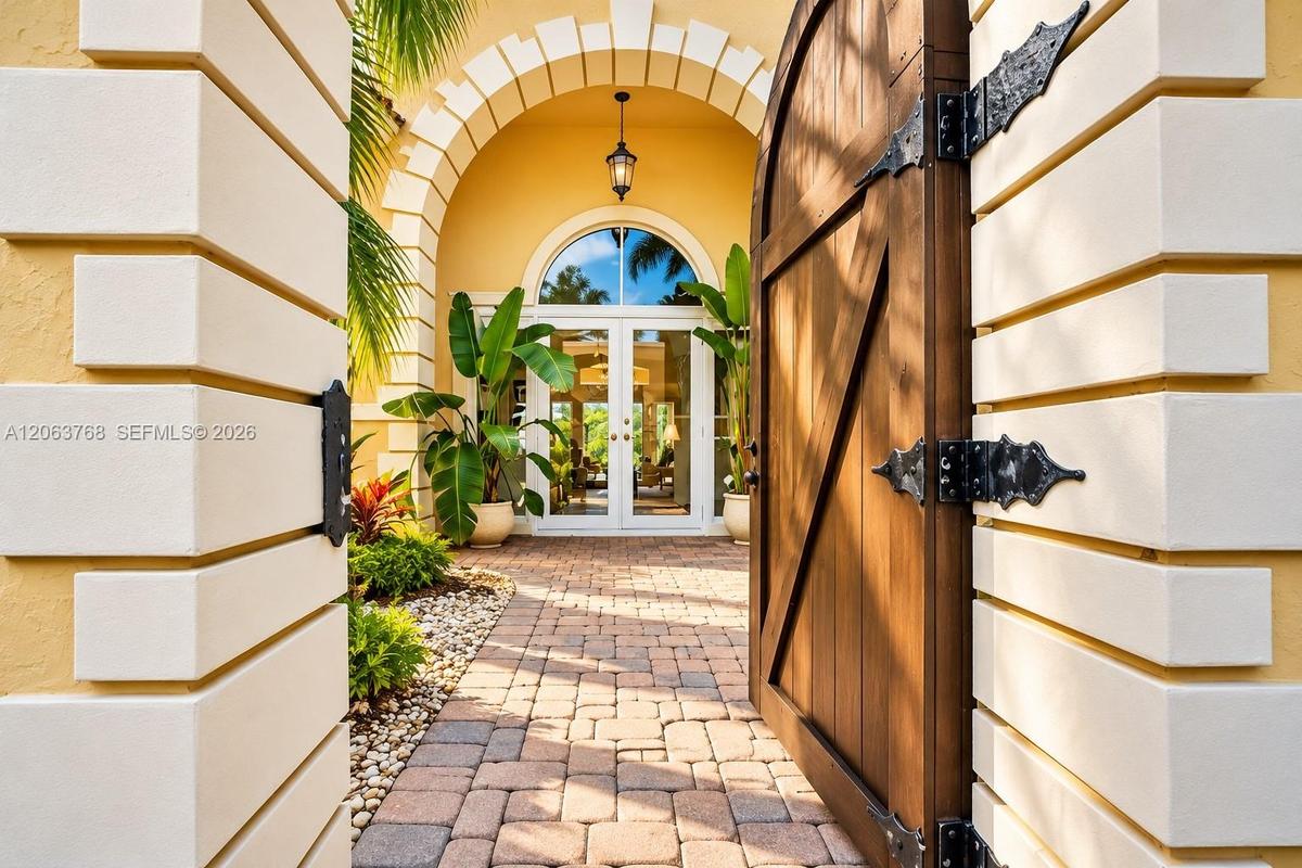 Entrance featuring a wooden arched gate with decorative iron hinges, masonry quoins, a paved stone walkway, and a covered portico with a transom-toppe