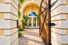 Entrance featuring a wooden arched gate with decorative iron hinges, masonry quoins, a paved stone walkway, and a covered portico with a transom-toppe