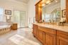 Custom wood cabinetry with integrated lighting, solid surface vanity countertop, undermount sink with brass-finish fixtures, tile flooring, and built-