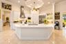 Gourmet kitchen featuring a central island with a solid-surface countertop, custom white cabinetry, stainless steel appliances, and a tray ceiling
