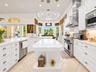 Kitchen featuring a large central island with solid-surface countertops, white shaker-style cabinetry, stainless steel professional-grade appliances, 