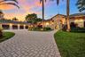 Stucco exterior residence featuring a four-car garage, arched entryways, tile roof, and a paver driveway set within a landscaped lot