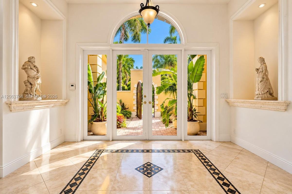 Entryway featuring double glass doors with a rounded transom window, polished stone tile flooring with a decorative geometric inlay, dual recessed wal