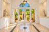 Entryway featuring double glass doors with a rounded transom window, polished stone tile flooring with a decorative geometric inlay, dual recessed wal