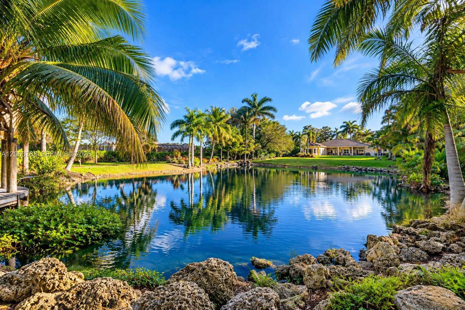 Waterfront property featuring a landscaped pond, rock hardscaping, and mature palm trees