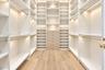 Custom walk-in closet featuring floor-to-ceiling white shelving, integrated recessed lighting, wood-finish flooring, and a central built-in chest of d