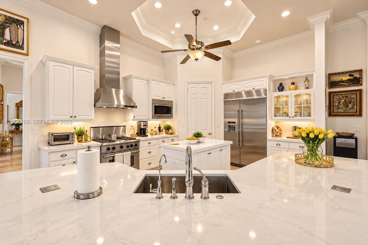 Gourmet kitchen featuring a large central island with a quartz countertop, stainless steel appliances, white cabinetry with glass-front display sectio