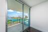 Floor-to-ceiling sliding glass door access to a covered balcony with a metal and glass railing, featuring tile flooring and hardwood-finish interior f