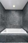 Built-in soaking tub featuring a white acrylic finish, surrounded by charcoal-toned stone tile surround and matching full-height tiled wall accents wi