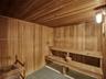 Sauna interior featuring natural wood-paneled walls and ceiling, multi-level tiered wooden benches, an integrated stone heater, and industrial-style w