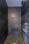 Walk-in shower enclosure featuring full-height charcoal stone tile walls, coordinating diamond-patterned tile flooring, a circular chrome showerhead, 